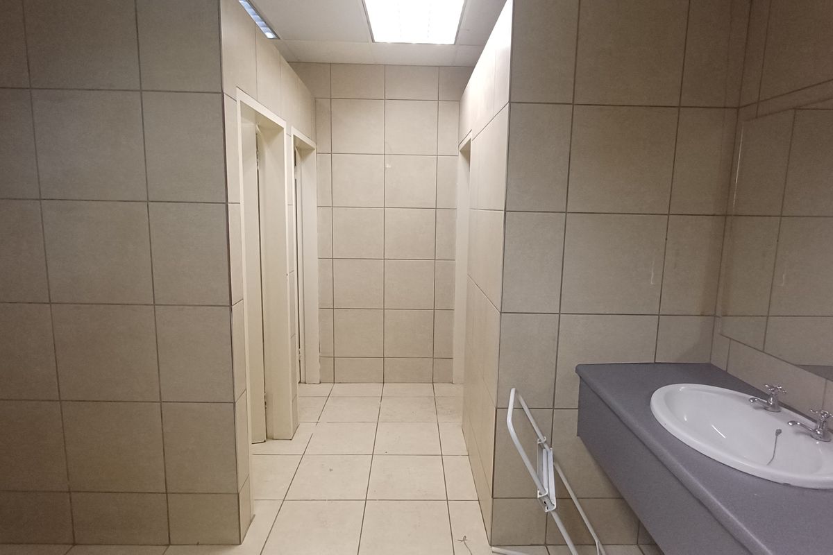A functional industrial restroom facility featuring tiled walls and flooring, a built-in vanity with a basin, and multiple stall access points.