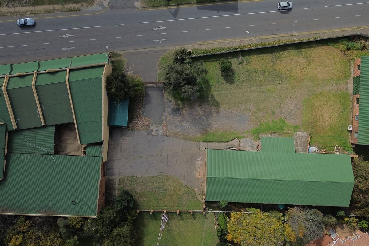 Aerial view of a commercial property featuring multiple buildings with green metal roofs, paved driveway areas, and surrounding grounds.