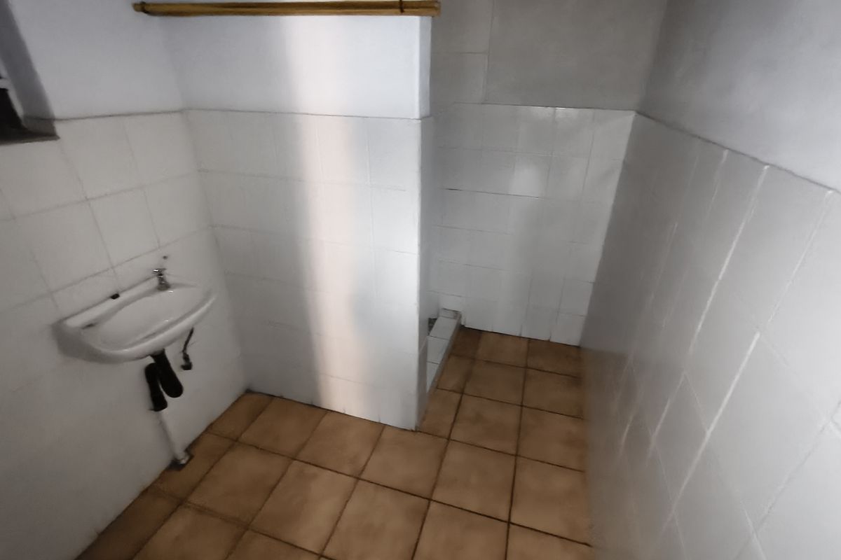 A basic, empty bathroom featuring a wall-mounted basin, tiled walls, and a shower area, requiring cosmetic updates to improve its overall condition.