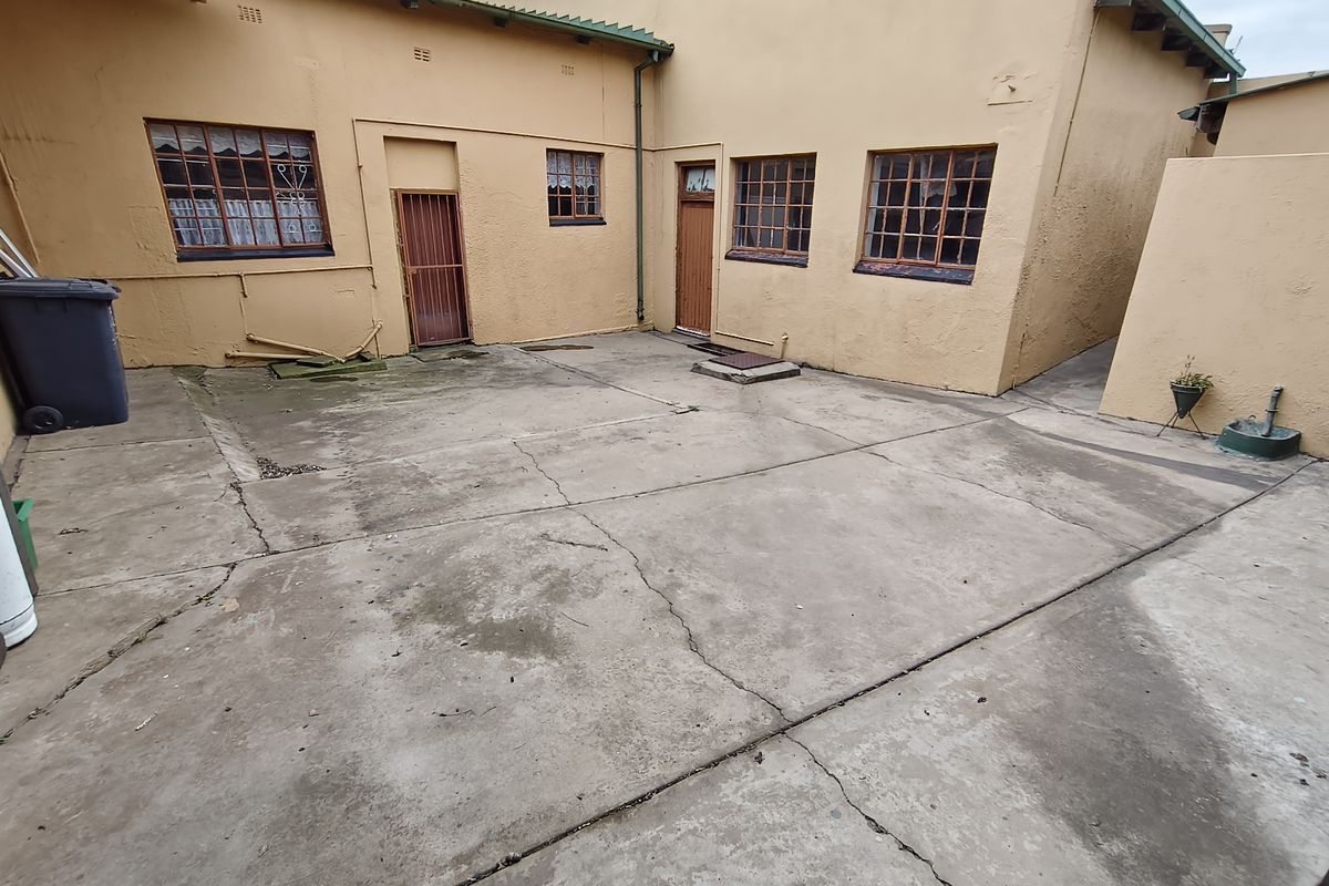 Rear exterior courtyard area featuring concrete paving, security-fitted windows, and access doors to the commercial building.