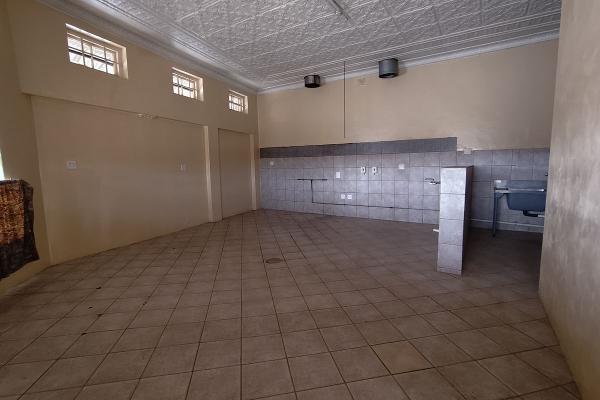 An empty commercial kitchen space featuring tiled flooring, a tiled splashback, a decorative pressed metal ceiling, and basic utility plumbing connections.