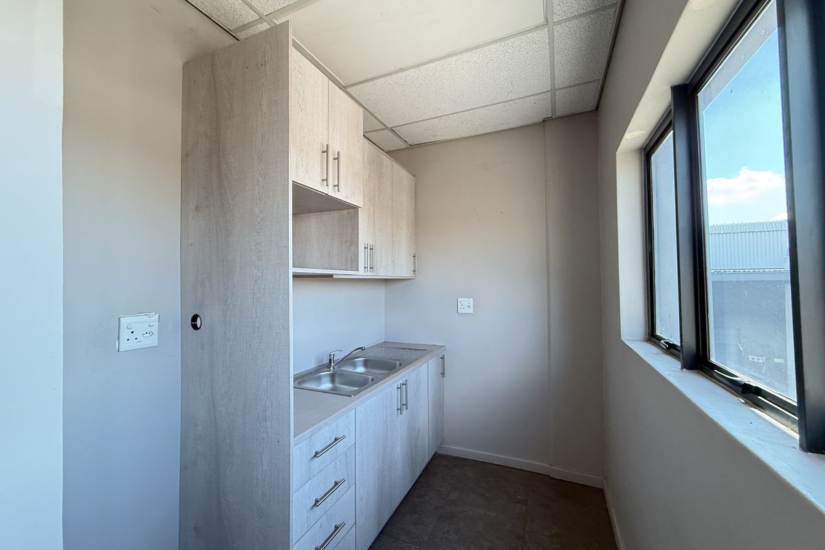 A functional kitchenette area featuring light wood-grain cabinetry, a stainless steel sink, and a drop ceiling, suitable for office or industrial utility use.