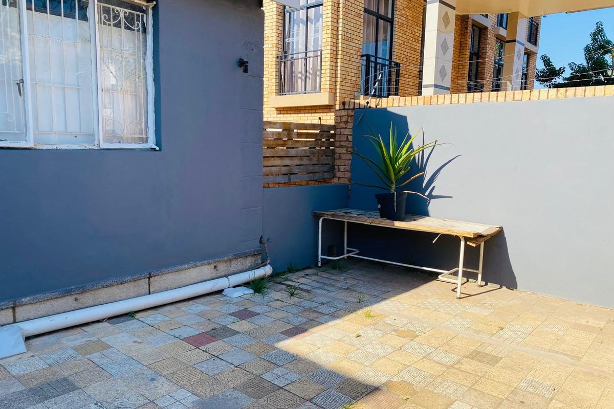 A paved outdoor courtyard area featuring a grey rendered wall, security window bars, and perimeter boundary walling.