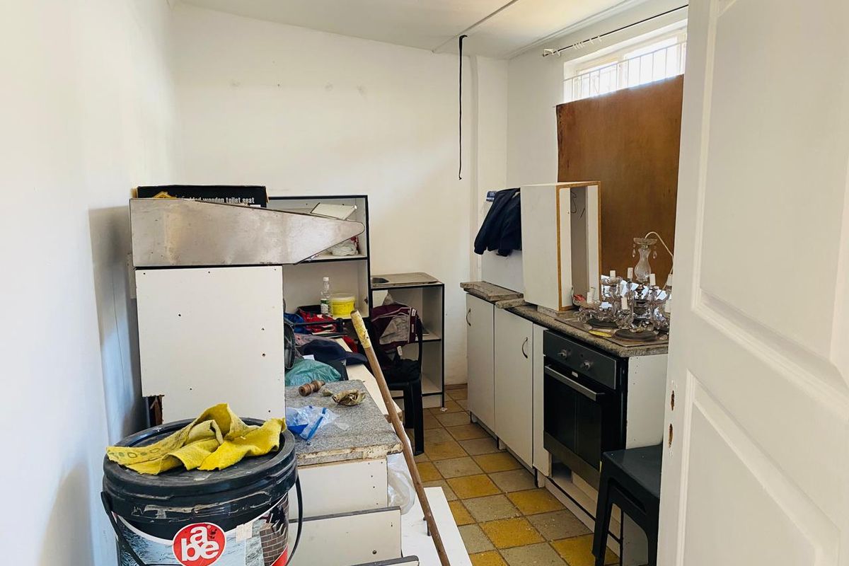 A small, dated kitchen area featuring basic cabinetry, a built-in oven, and tiled flooring, currently in need of significant renovation and repair.