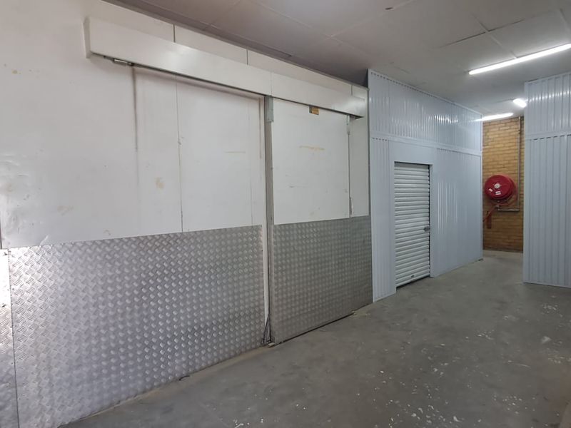 Industrial utility space featuring a large sliding cold storage door, roller shutter access, metal wall cladding, and durable concrete flooring.