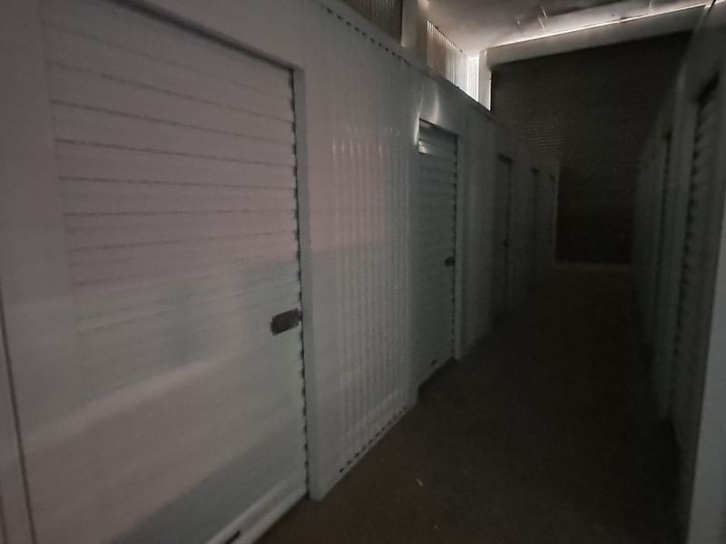 A corridor within an industrial storage facility featuring multiple individual metal roller shutter storage units and concrete flooring.