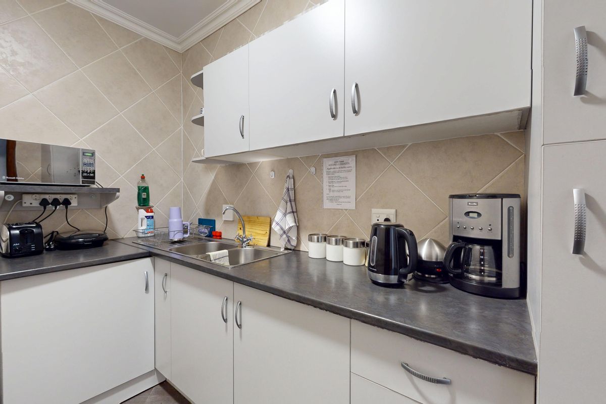 A functional kitchen area featuring white cabinetry, dark laminate countertops, a stainless steel sink, and a neutral tiled backsplash.