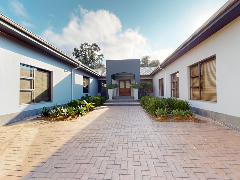 A well-maintained commercial property entrance featuring a paved driveway, landscaped garden beds, and a covered portico leading to a double door entry.