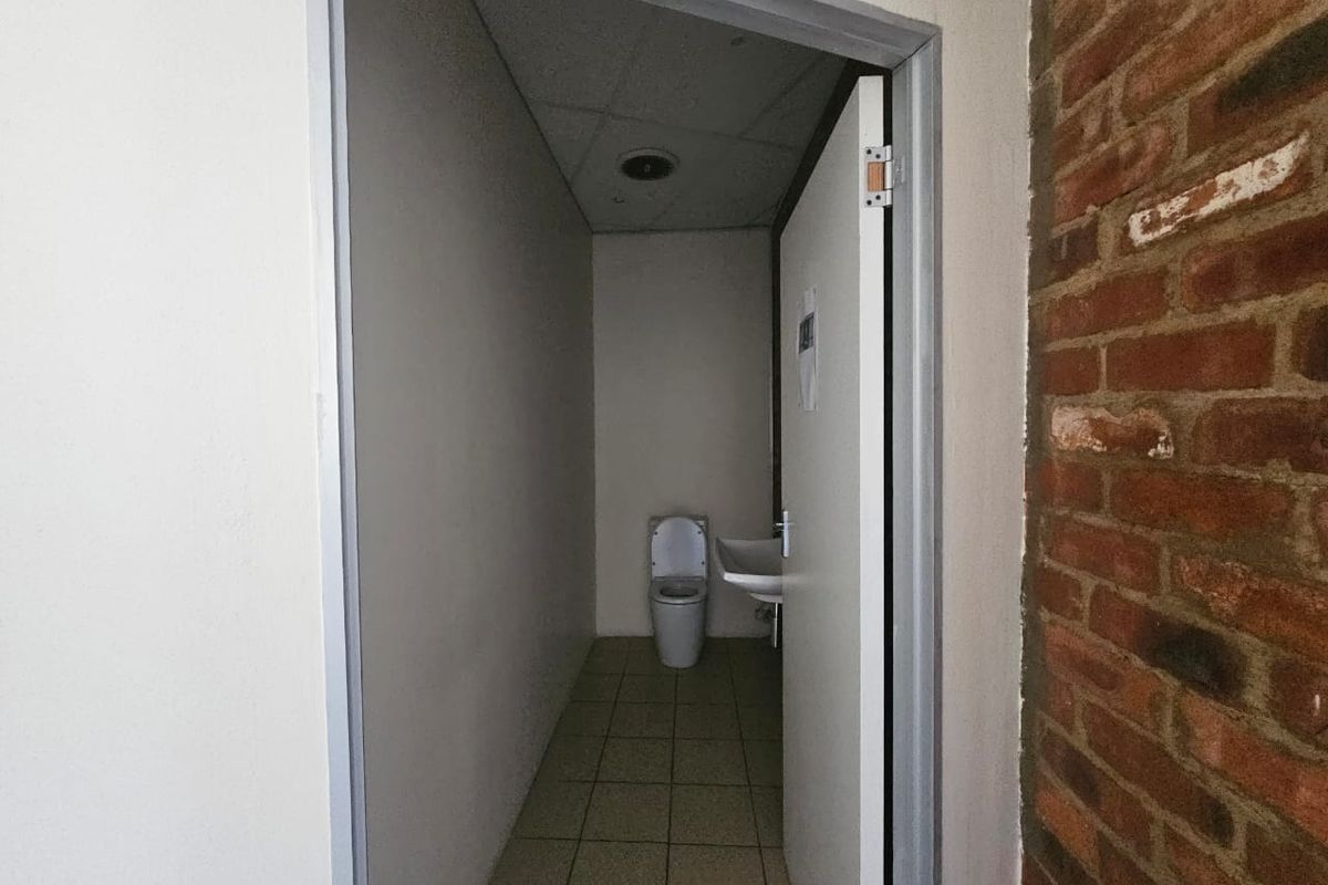 A compact, functional bathroom featuring a toilet and wall-mounted basin, characterized by simple finishes and an adjacent exposed brick wall.