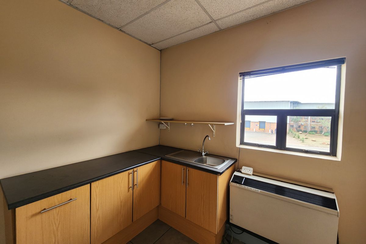 A functional kitchenette area featuring wood-look cabinetry, a stainless steel sink, laminate countertops, and a wall-mounted air conditioning unit.