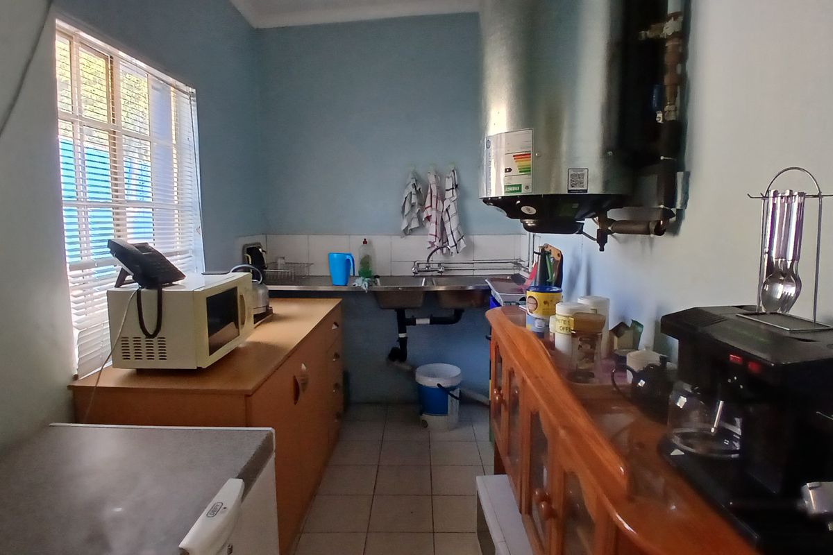 A functional office kitchenette featuring a double stainless steel sink, tiled flooring, and a wall-mounted electric water heater.
