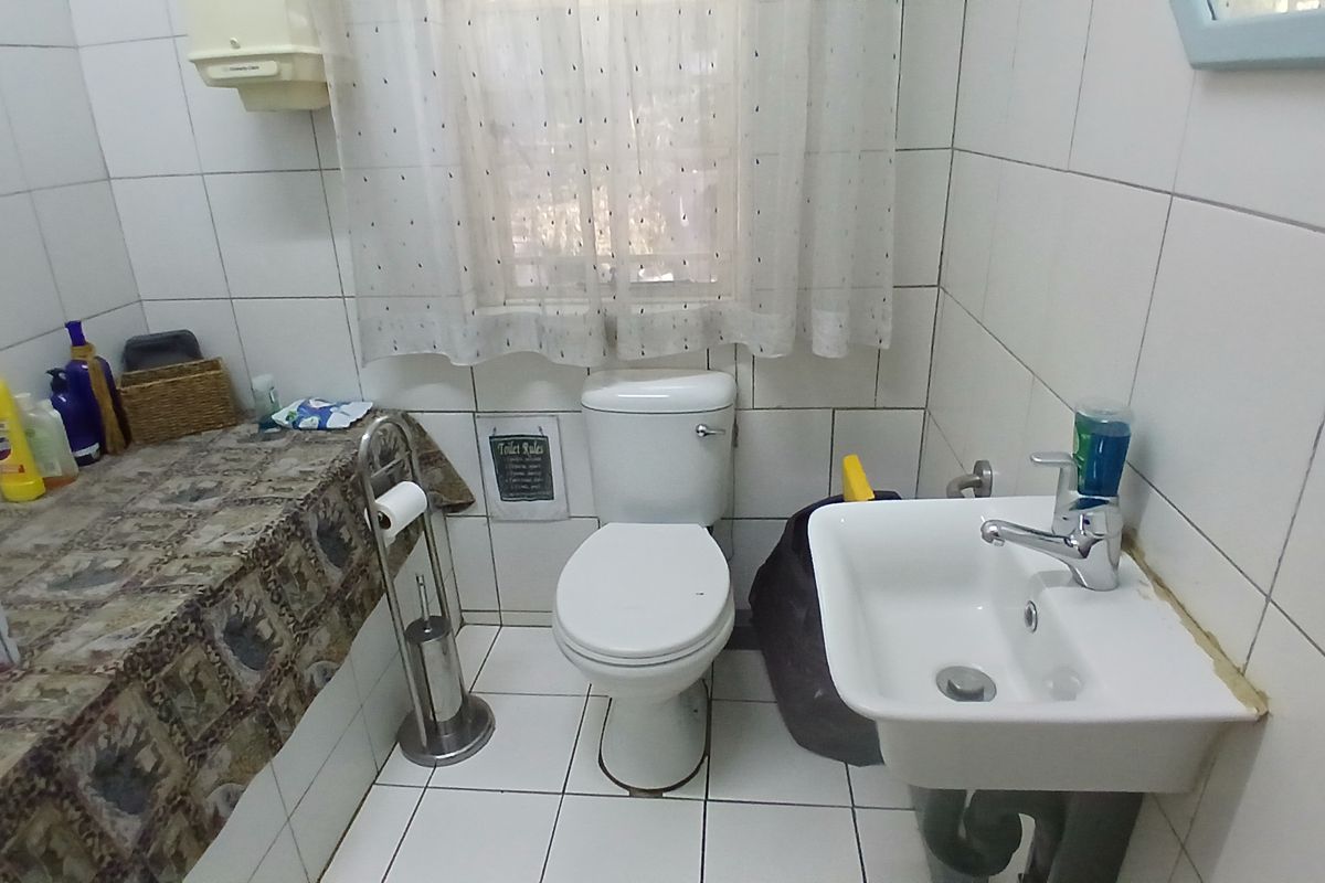 A compact office bathroom featuring white ceramic wall and floor tiles, a standard toilet, and a wall-mounted basin with a chrome mixer tap.