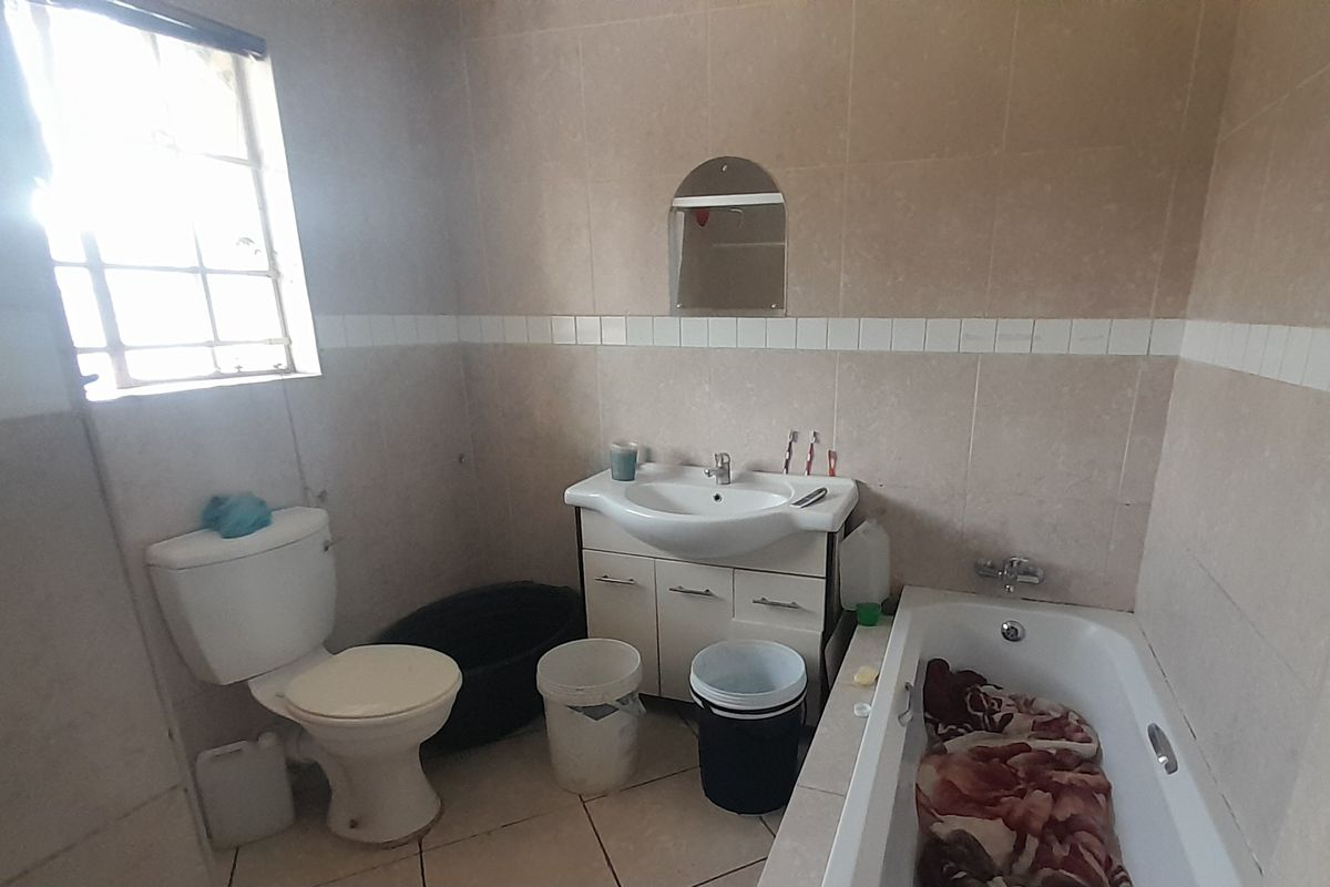 A functional bathroom featuring a vanity basin, toilet, and bathtub with tiled finishes, requiring some maintenance and cosmetic updates.