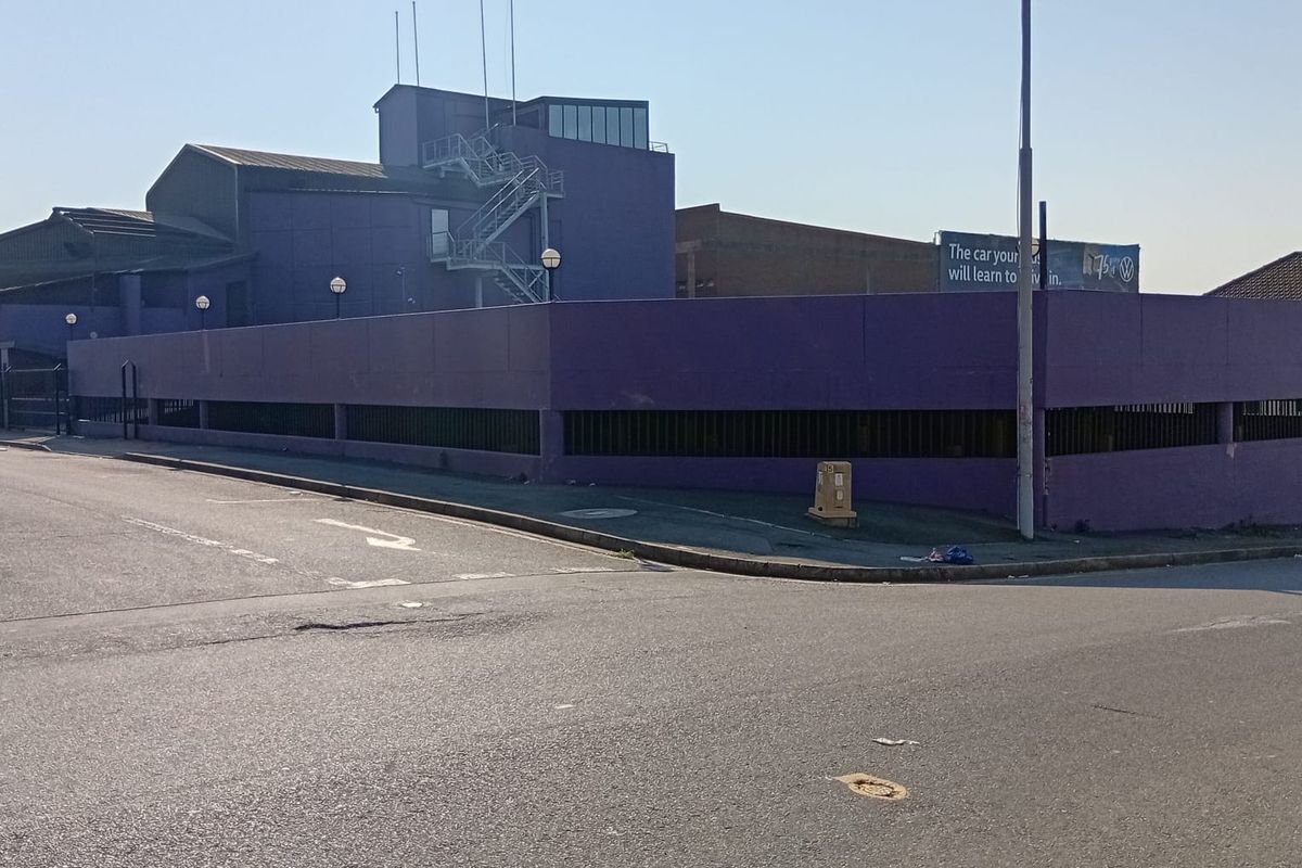 Street view of a commercial property featuring a prominent purple boundary wall, external metal staircase, and adjacent asphalt road access.