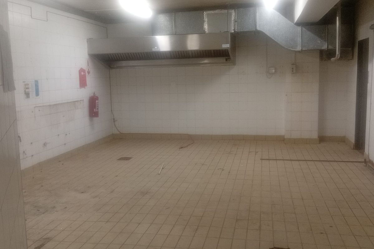 A vacant commercial kitchen space featuring tiled walls and flooring, equipped with a stainless steel extractor canopy and integrated ventilation ducting.