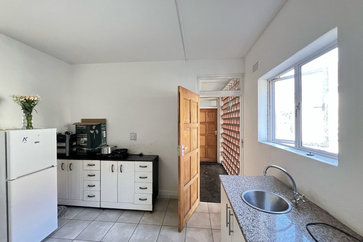 A functional kitchen featuring white cabinetry, granite-look countertops, a stainless steel sink, and tiled flooring, with direct access to an external walkway.