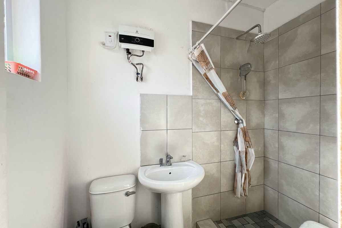 Compact bathroom featuring a pedestal sink, toilet, and a tiled shower area with an overhead shower head and wall-mounted water heater.