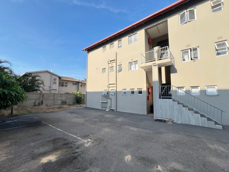 Exterior view of an apartment building featuring a paved parking area, external stairwell, and functional fire safety equipment.
