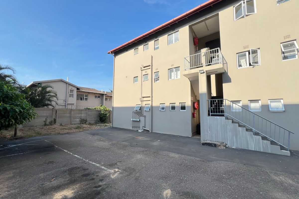 Exterior view of an apartment building featuring a paved parking area, external stairwell, and functional fire safety equipment.