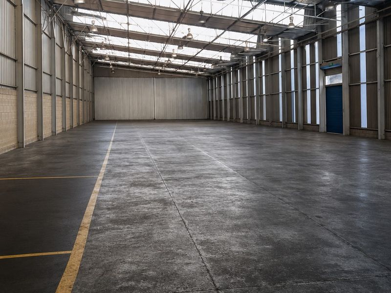 Spacious industrial warehouse unit featuring high ceilings, concrete flooring, ample natural light through skylights, and robust steel frame construction.