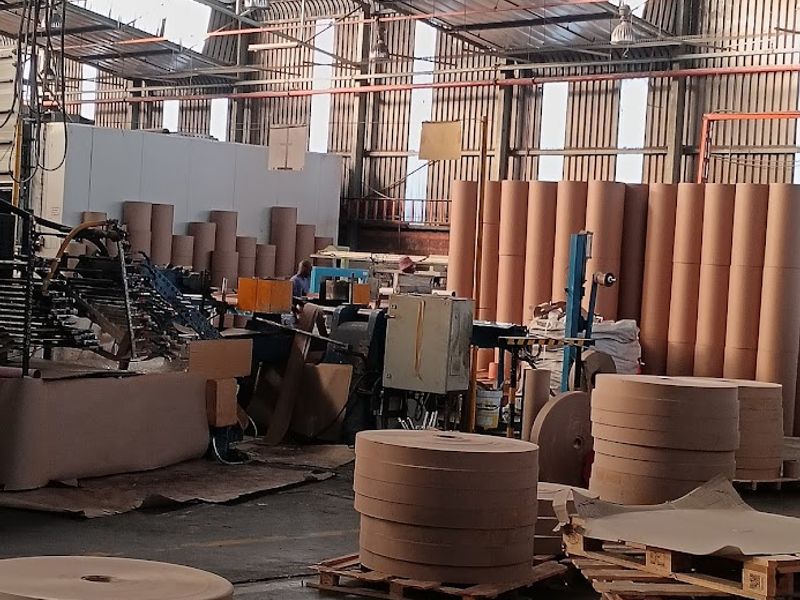 Industrial warehouse space featuring high ceilings with exposed steel trusses, corrugated metal walls, and concrete flooring, currently utilized for paper roll storage and processing.