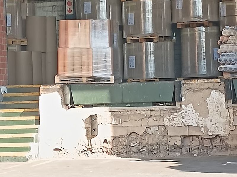 Industrial loading dock area featuring a concrete retaining wall with visible structural wear and metal access stairs.