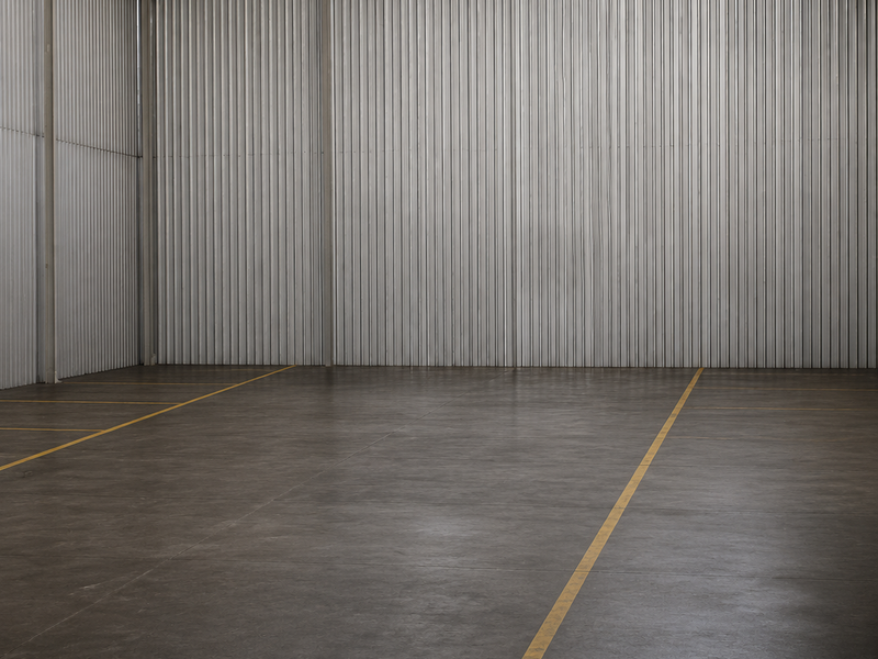 Spacious industrial warehouse interior featuring high ceilings with skylights, corrugated metal walls, polished concrete flooring, and functional industrial pendant lighting.