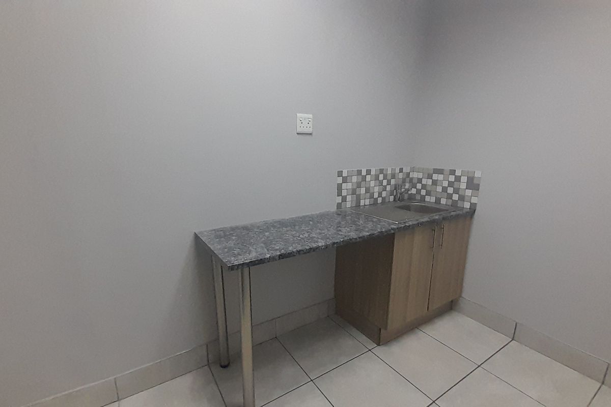 A compact kitchenette area featuring built-in cabinetry, a laminate countertop, a stainless steel sink, and a decorative mosaic tile backsplash.