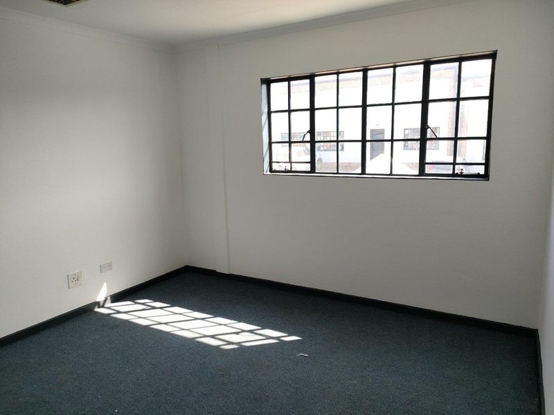 A vacant office space featuring neutral walls, dark carpeting, and a large industrial-style steel-framed window providing natural light.