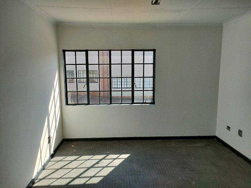 An empty office space featuring industrial-style steel-framed windows, textured rubber flooring, and neutral walls, suitable for a professional workspace.