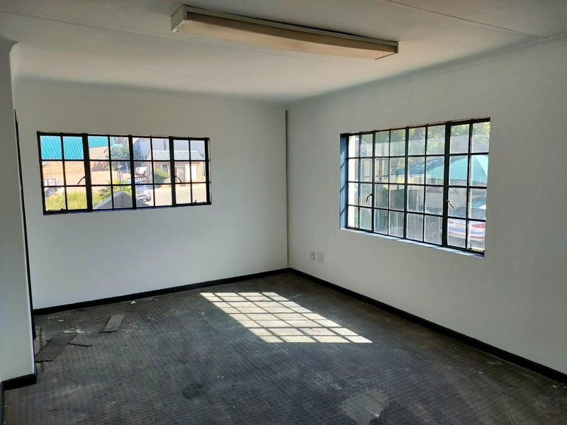 An empty office space featuring industrial-style steel-framed windows, fluorescent lighting, and worn flooring, suitable for a workshop or commercial workspace.