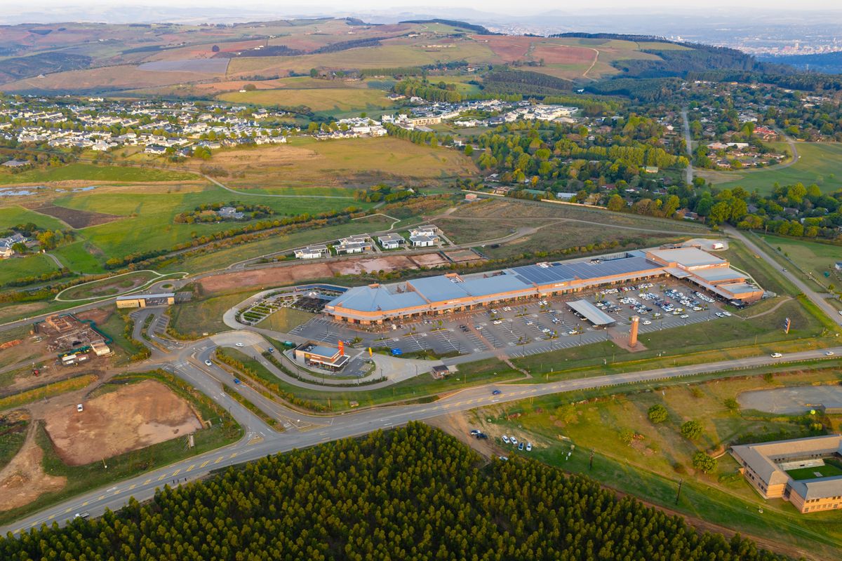 Aerial view of a large retail shopping center featuring extensive parking facilities and surrounding landscaped grounds in a suburban setting.