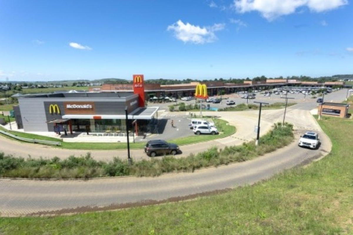Aerial view of a retail center featuring a standalone fast-food restaurant, extensive parking facilities, and paved access roads.