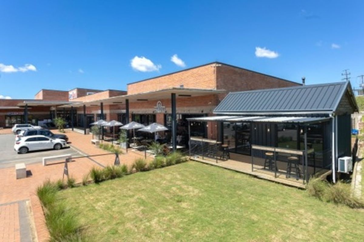 A well-maintained retail complex featuring brick facades, covered outdoor seating areas, and a landscaped lawn with paved pedestrian access.
