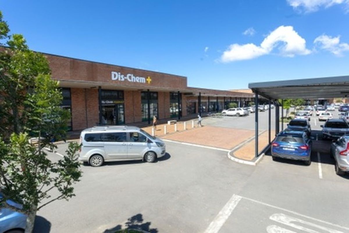 Exterior view of a retail shopping center featuring a brick facade, storefront signage, and a paved parking area with covered parking bays.