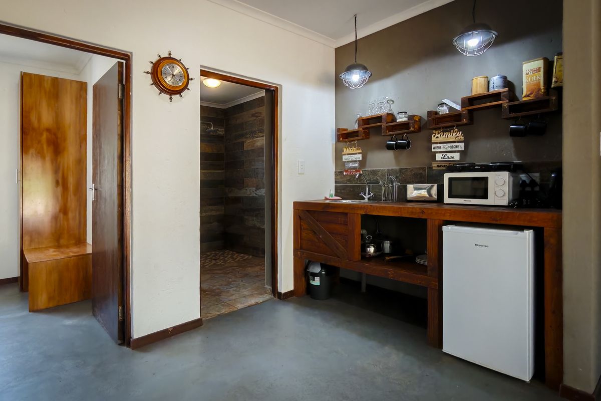 A compact kitchenette area featuring rustic wooden cabinetry, open shelving, and a sink, with direct access to an adjacent bathroom.