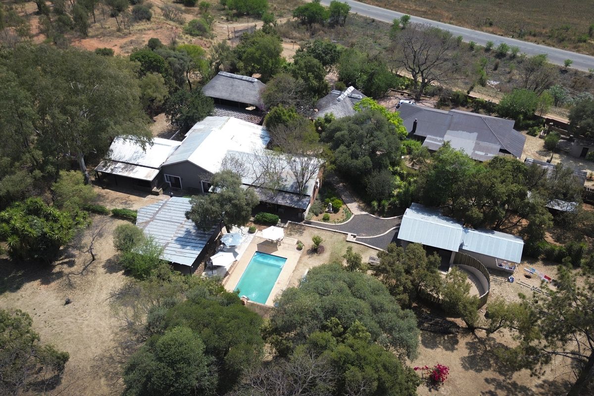 Aerial view of a farm property featuring multiple buildings, a swimming pool, and established trees set within a rural landscape.