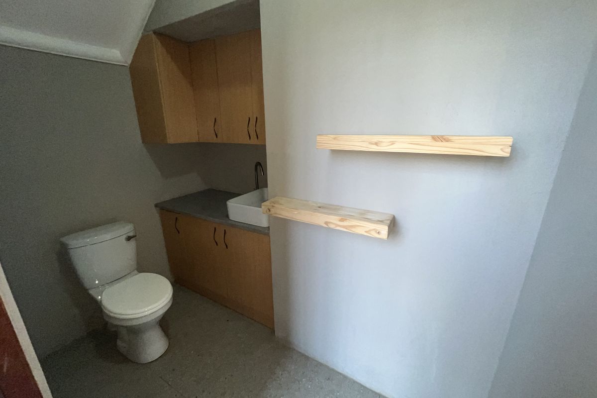 A functional office bathroom featuring built-in wooden cabinetry, a sink, a toilet, and wall-mounted floating shelves.