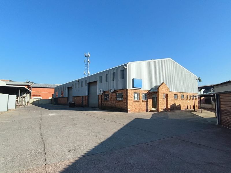 Industrial warehouse exterior featuring a corrugated metal roof, face brick walls, and a large roller shutter door, set within a paved yard area.