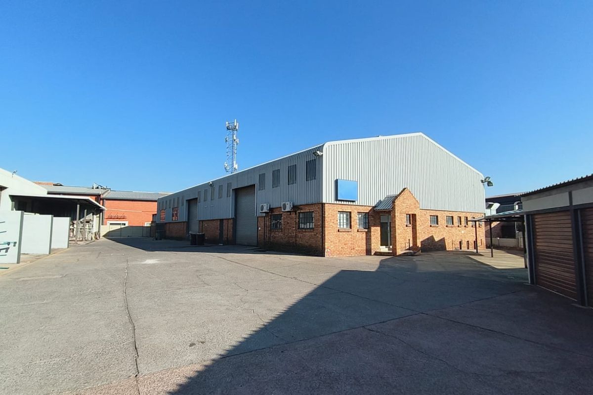 Industrial warehouse exterior featuring a corrugated metal roof, face brick walls, and a large roller shutter door, set within a paved yard area.
