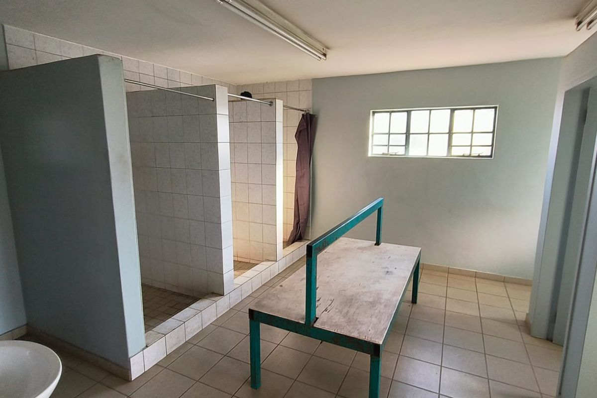 Industrial-style communal bathroom facility featuring multiple tiled shower cubicles, ceramic flooring, and functional lighting, suitable for renovation or modernization.