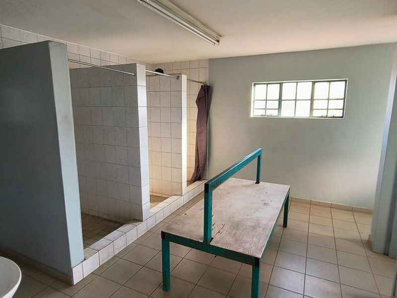 Industrial-style communal bathroom facility featuring multiple tiled shower cubicles, ceramic flooring, and functional lighting, suitable for renovation or modernization.