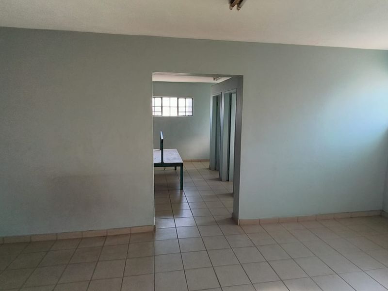 An empty, functional office space featuring tiled flooring and natural light from grid windows, suitable for a variety of industrial or commercial uses.
