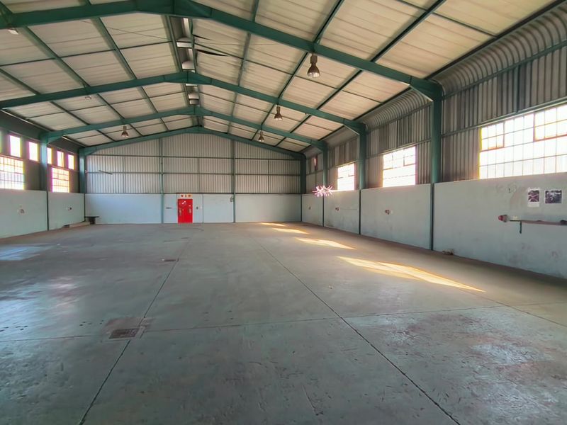 Spacious industrial warehouse featuring a high-clearance steel portal frame, concrete flooring, and ample natural light through steel-framed windows.