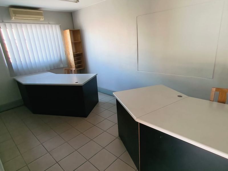 A functional office space featuring tiled flooring, vertical blinds, and a wall-mounted air conditioning unit.