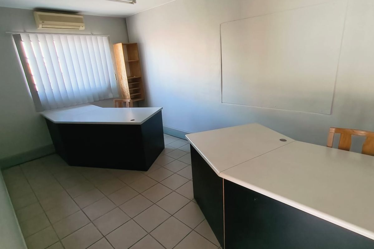 A functional office space featuring tiled flooring, vertical blinds, and a wall-mounted air conditioning unit.