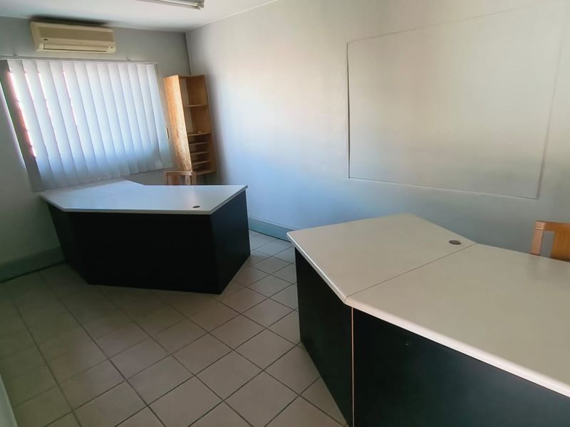 A functional office space featuring tiled flooring, a wall-mounted air conditioning unit, and vertical blinds, providing a practical environment for professional use.