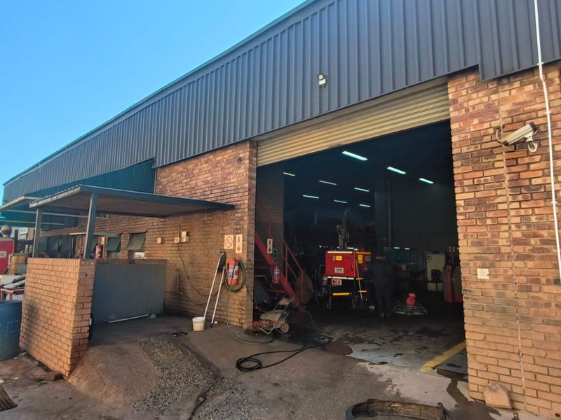 Front elevation of a retail or industrial unit featuring a large roller shutter door, brick facade, and metal roof cladding.