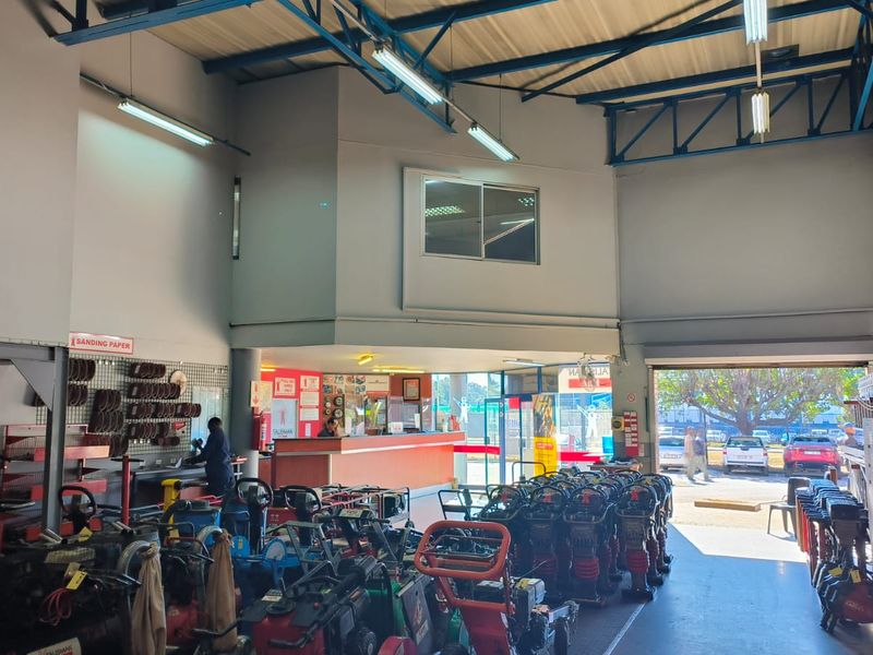 Spacious retail utility and equipment rental area featuring high ceilings with exposed steel trusses, a service counter, and large roller shutter access.