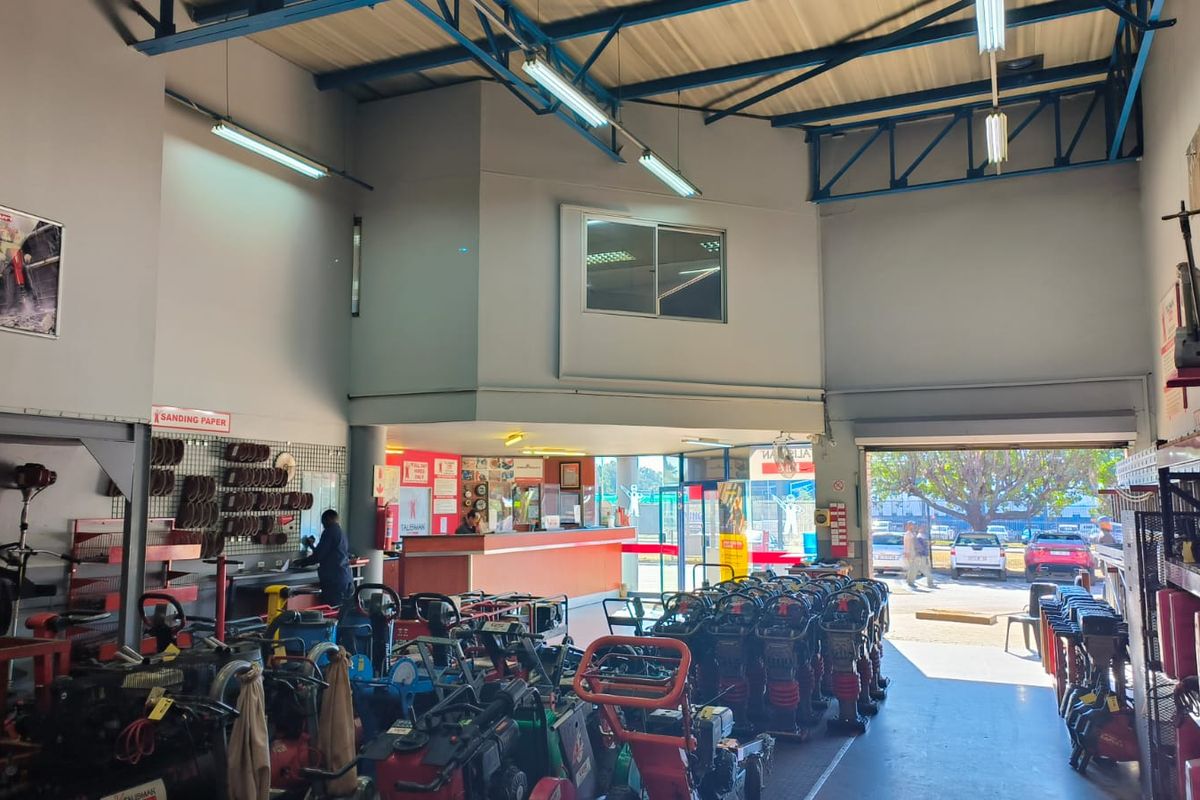 Spacious retail utility and equipment rental area featuring high ceilings with exposed steel trusses, a service counter, and large roller shutter access.